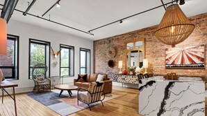 Uma sala de estar moderna com parede de tijolos, janelas amplas e piso de madeira.