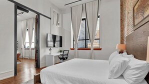 Habitación de hotel moderna con una cama grande, un escritorio, un televisor y vistas de la ciudad desde la ventana.