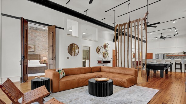 Een ruime woonkamer met een leren bank, houten stoelen, een salontafel en een pooltafel.