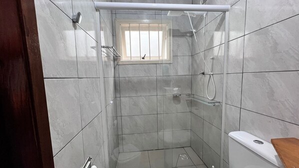 Un baño pequeño con azulejos, ducha, inodoro y ventana.