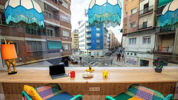 A room with a wooden desk, two colorful chairs, a laptop, a red mug, and a yellow mug. - Guesthome Lemon & Green (Granada)