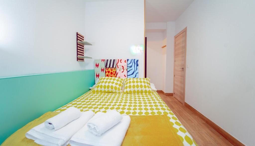A single bed with a yellow and white checkered bedspread, two pillows, and two neatly folded white towels.