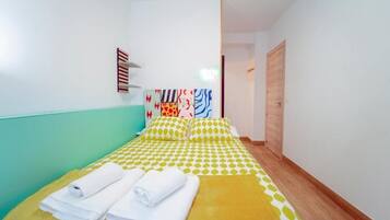 A single bed with a yellow and white checkered bedspread, two pillows, and two neatly folded white towels.