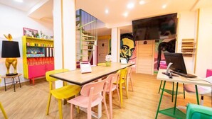 A brightly colored room with a wooden table, colorful chairs, a bookshelf, and a mural on the wall. - Guesthome Lemon & Green (Granada)