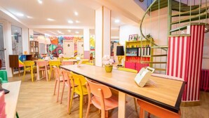 A brightly lit indoor space with a long wooden table and colorful chairs, surrounded by shelves and a spiral staircase. - Guesthome Lemon & Green (Granada)