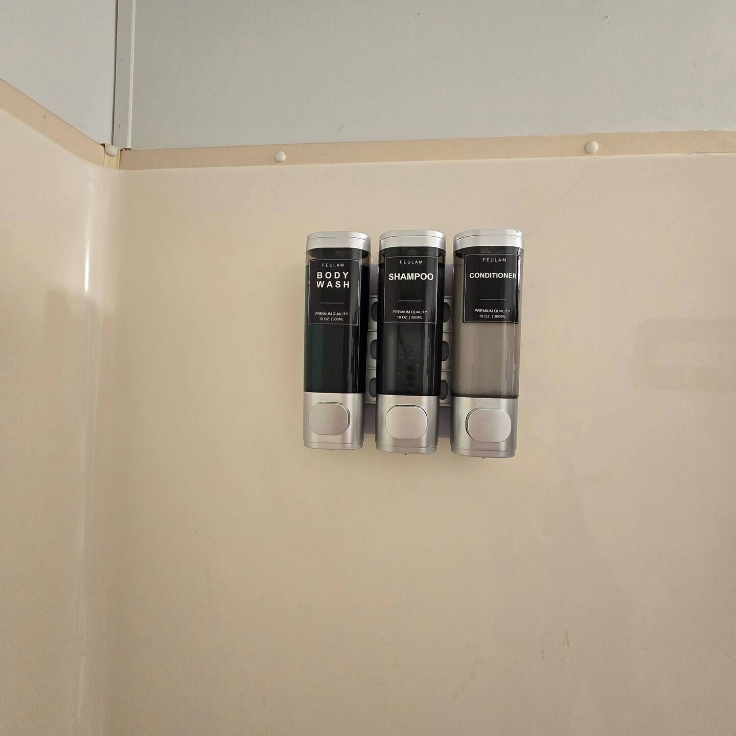 Een wanddispenser met drie flessen Feulam bodywash, shampoo en conditioner.