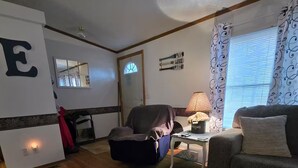 Una sala de estar con un sofá gris, un sillón negro, una mesita con una lámpara y una ventana con cortinas estampadas.