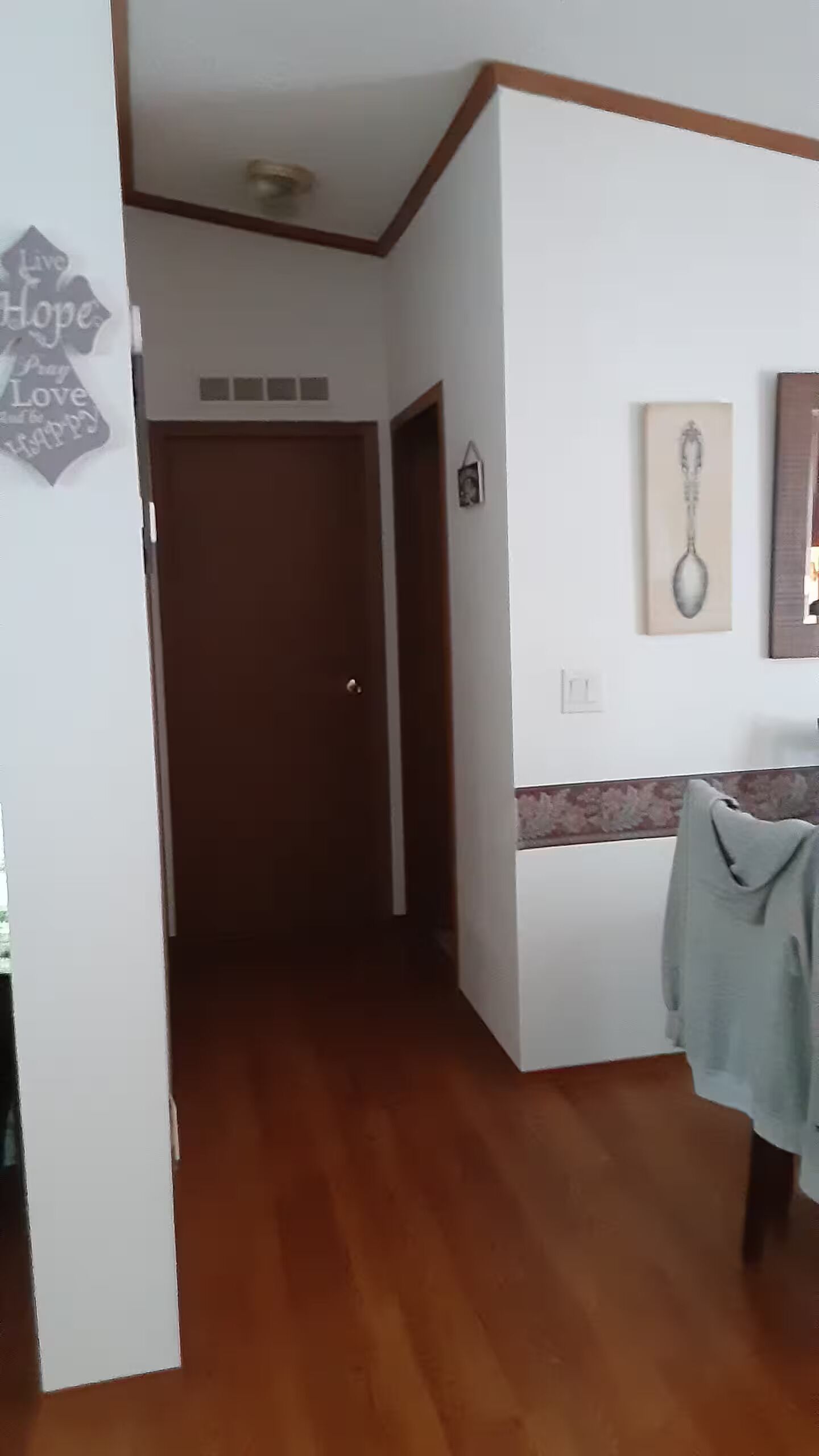 Ein Zimmer mit Holzboden, einer Tür, einem an der Wand montierten Lichtschalter und einem gerahmten Bild.