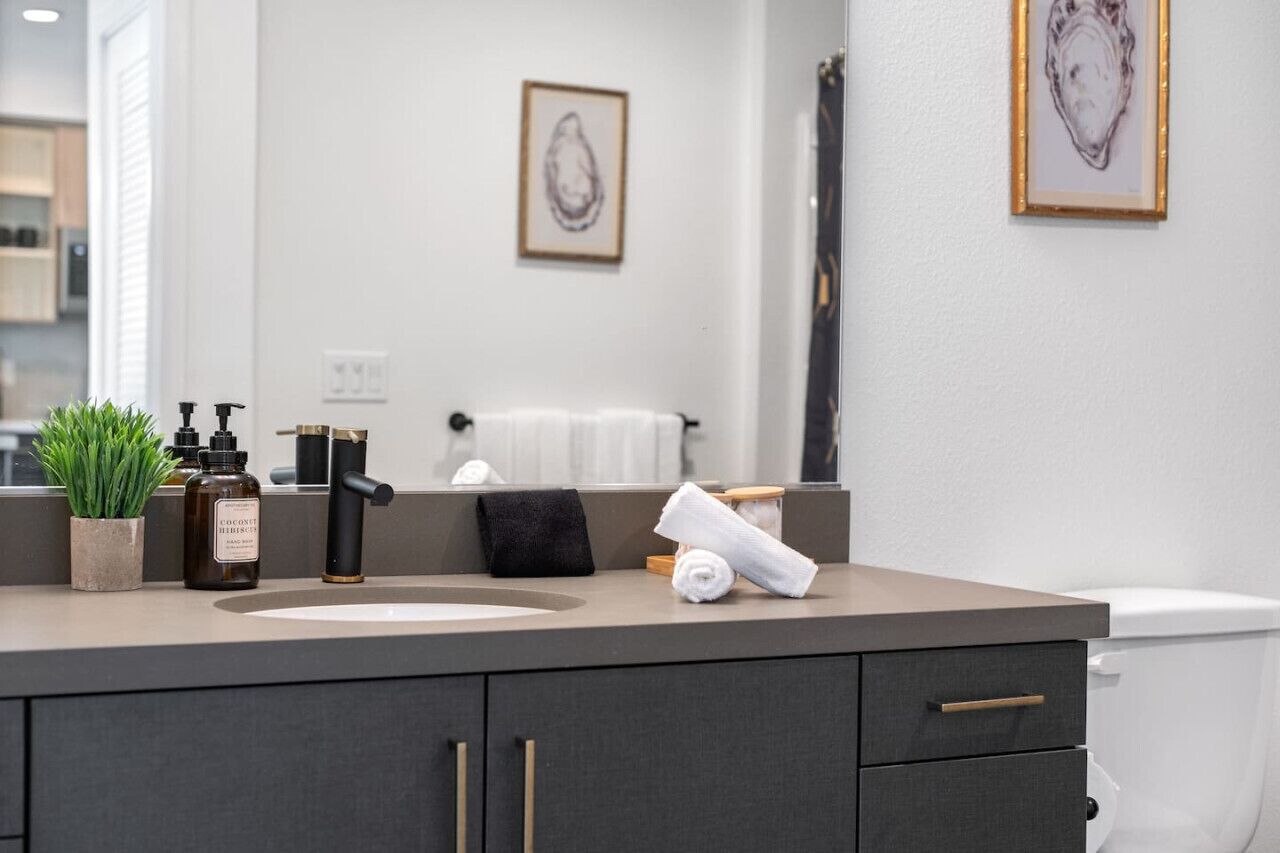 Un baño moderno con un tocador gris, un inodoro blanco y una obra de arte enmarcada en la pared.