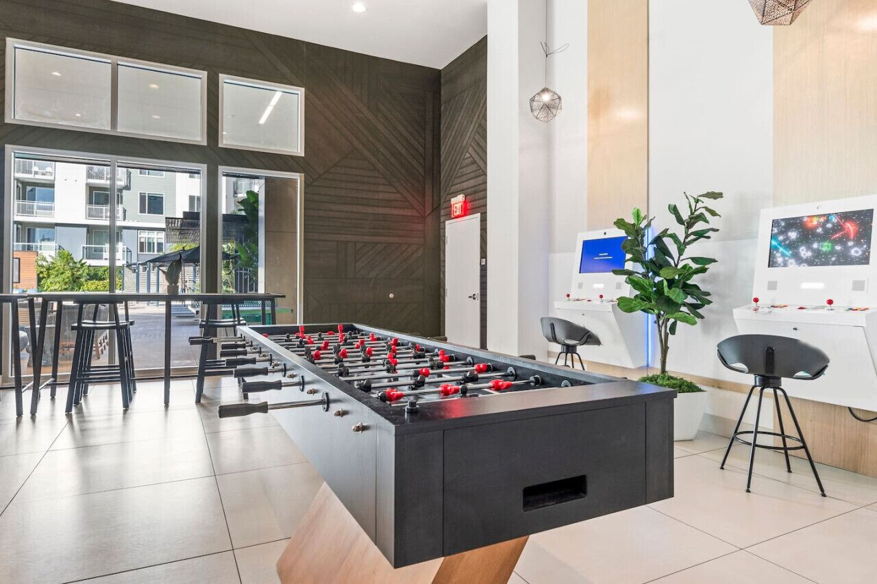 A modern indoor space with a foosball table, a reception desk, and a digital screen.