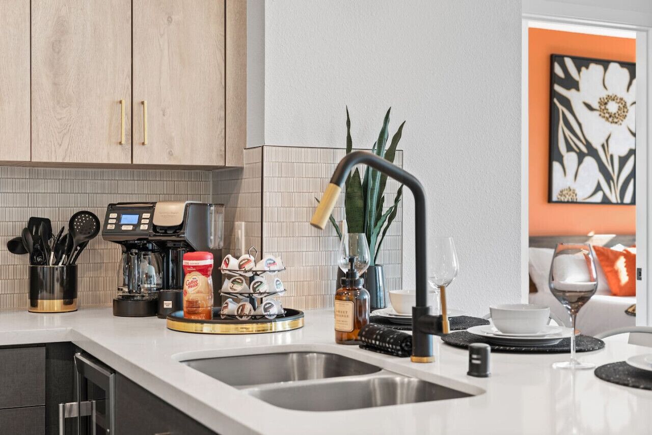 A modern kitchen with a coffee machine, a tray of coffee pods, a coffee grinder, and a sink.