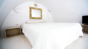 A white room with a bed, a wall-mounted mirror, and a TV. - Akrotiri Castle View (Santorini)