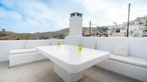 A white outdoor seating area with a table and two yellow candle holders, overlooking a hillside with white buildings. - Akrotiri Castle View (Santorini)
