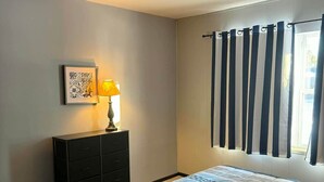 A bedroom with a bed, a dresser, a lamp, and a window with curtains.