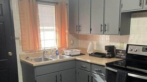 A kitchen with grey cabinets, a stainless steel oven, a coffee maker, and a window with orange curtains.