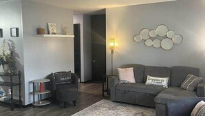 A modern living room with a grey sofa, a patterned rug, and a wall-mounted lamp.