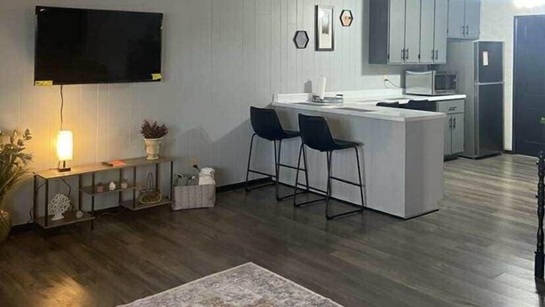 A modern kitchen with a central island, bar stools, a flat-screen TV, and a microwave.