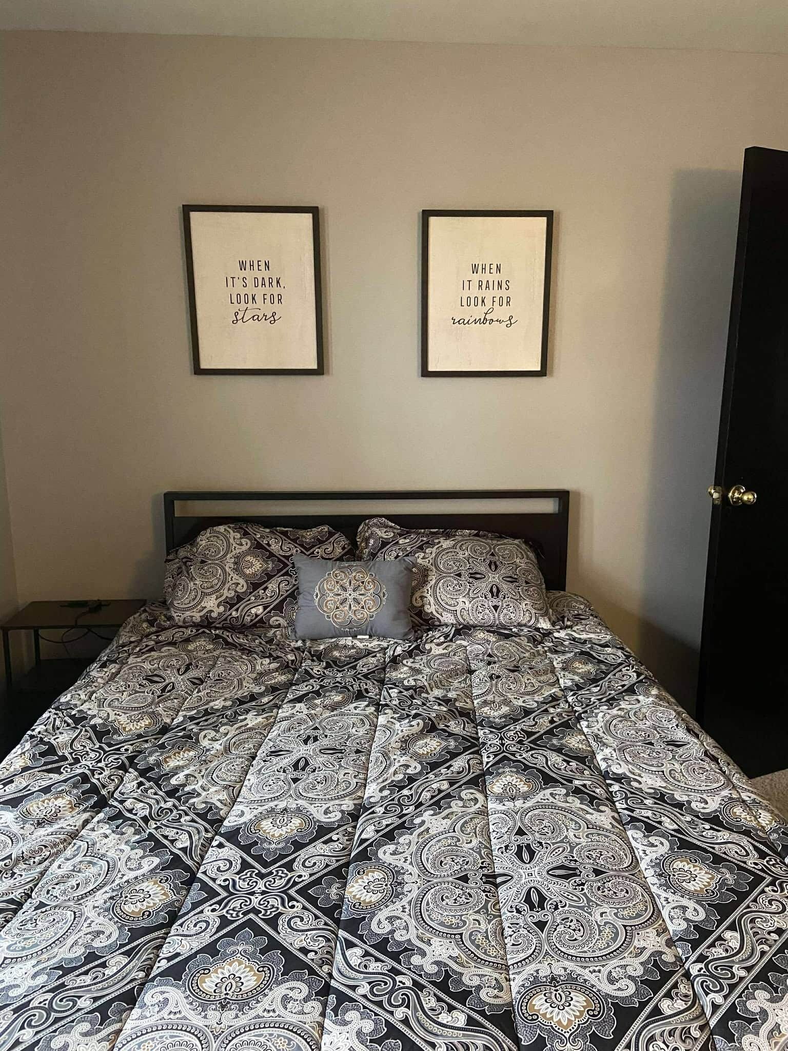 Un dormitorio con una cama, dos citas enmarcadas en la pared y una puerta.