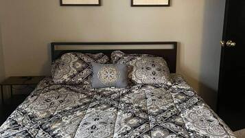 Un dormitorio con una cama, dos citas enmarcadas en la pared y una puerta.