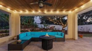 A covered patio area with a sectional sofa, a round table with a fire feature, and a ceiling fan. - Palm Haven (New Smyrna Beach)