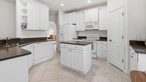 A kitchen with white cabinets, a granite countertop, a built-in microwave, and a refrigerator. - Palm Haven (New Smyrna Beach)