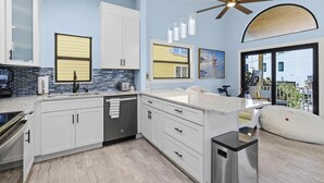 Eine moderne Küche mit weißen Schränken, einem Einbauofen und einem Geschirrspüler. Es gibt eine große Kücheninsel mit Spüle und Deckenventilator.