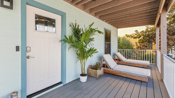 Eine überdachte Veranda mit Holzboden, eine weiße Tür mit Fenster und ein Blumentopf.