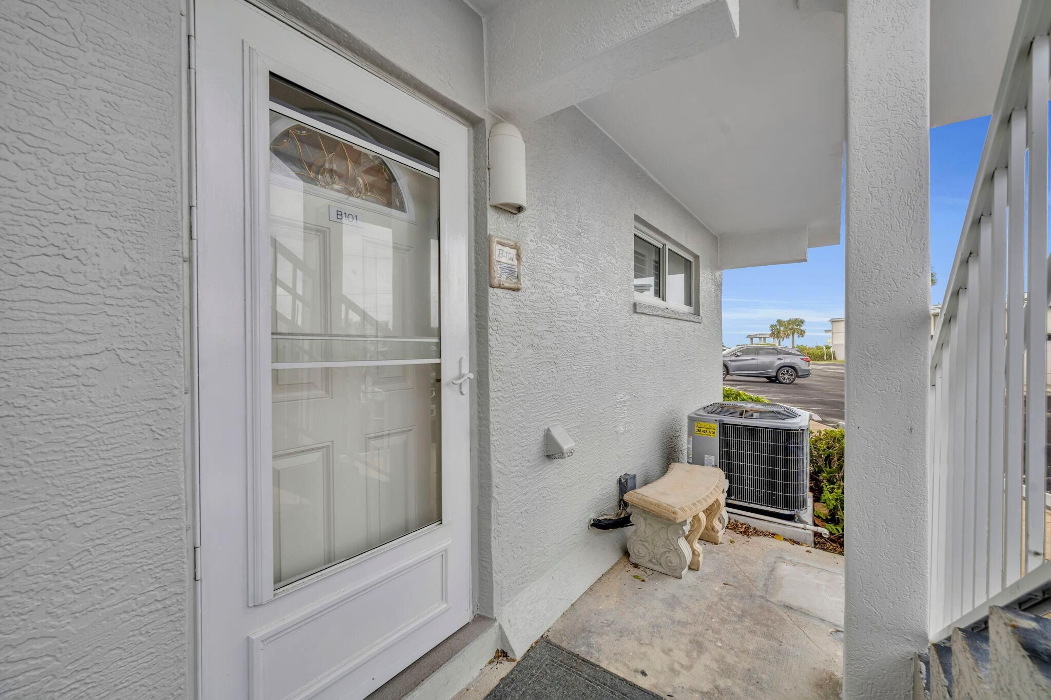 A white exterior with a glass door, a small bench, and an air conditioning unit.
