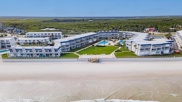 Hotel a primera línia de platja amb diversos edificis, zona de piscina i platja al primer pla.