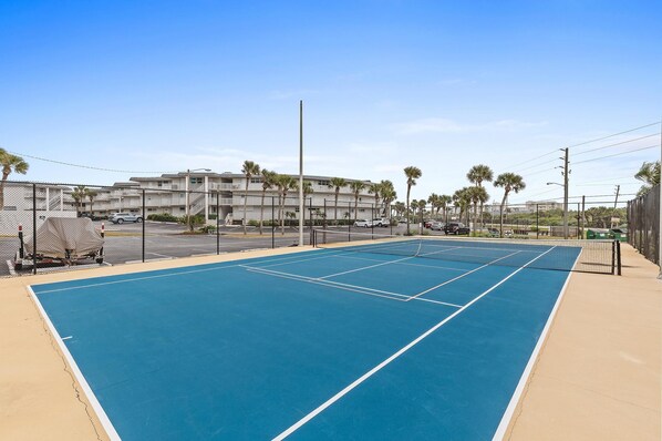 A tennis court with a net, surrounded by a fence, and palm trees in the background. - Southeaster B101 (New Smyrna Beach)