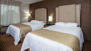Ein Hotelzimmer mit zwei Betten, einem Fenster mit Vorhängen, einem Nachttisch mit Lampe und einem Wandheizkörper.