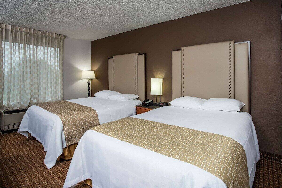 Une chambre d’hôtel avec deux lits, une fenêtre avec des rideaux, une table de chevet avec une lampe et un radiateur fixé au mur.