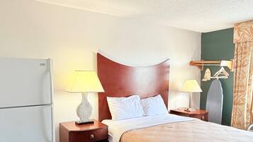 A hotel room with a bed, two bedside tables, a lamp, a mirror, a coat rack, and a refrigerator.