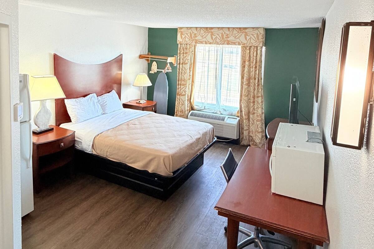 Une chambre d’hôtel équipée d’un lit, d’un bureau, d’une chaise, d’une lampe et d’un appareil de climatisation.