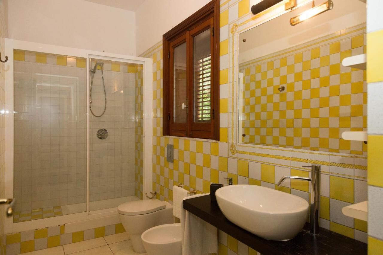 Une salle de bain avec une douche à parois de verre, des toilettes blanches, un lavabo avec un miroir et des carreaux jaunes et blancs formant un motif à damier.