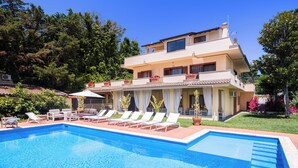 Ein zweistöckiges Haus mit Swimmingpool, Liegestühlen und einer überdachten Terrasse.