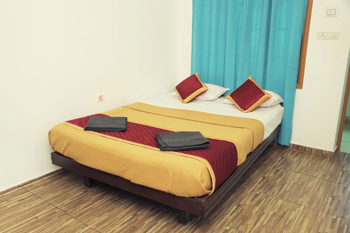 A neatly made bed with a yellow and red bedspread, two pillows, and two folded blankets.