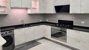 Une cuisine moderne avec des meubles gris, un plan de travail noir, un lave-linge encastré et une cuisinière.