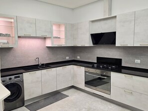 A modern kitchen with grey cabinets, a black countertop, a built-in washing machine, and a stove. - Family-Friendly & Warm  2 bedroom apartment  . Best for vacationers (Amman)