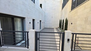 Une ruelle étroite, fermée par un portail, bordée de murs blancs et d’une grille en métal noir.
