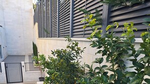 Un bâtiment moderne avec un rez-de-chaussée carrelé et un balcon agrémenté de plantes en pot et d’un petit arbre.