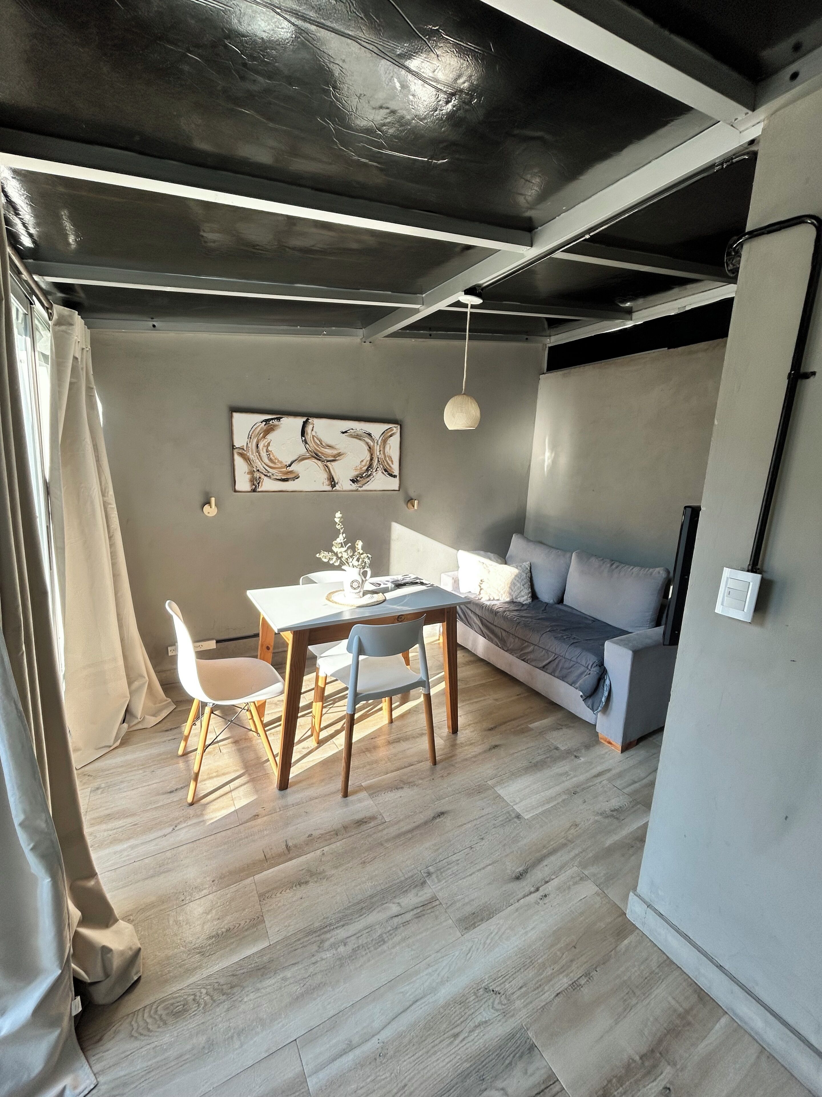 Un espacio moderno de estar con comedor, sofá y un cuadro en la pared.