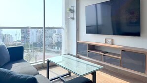 Una sala de estar moderna con televisor grande, mesa de centro de vidrio y un sofá.
