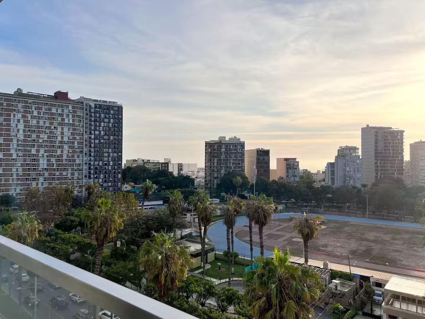 A cityscape with high-rise buildings, palm trees, and a large open area.