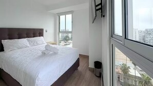 Un dormitorio moderno con una cama grande, vista de la ciudad a través de un ventanal y una lámpara en el techo.