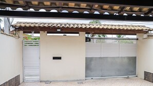 A covered outdoor area with a tiled floor, a white wall, and a metal gate. - Casa de Praia Pet Friendly com Churrasqueira e Ar (Rio das Ostras)