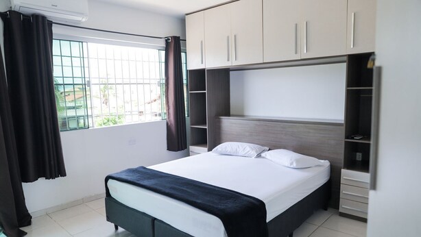 A modern bedroom with a bed, built-in wardrobe, and a window with curtains. - Casa de Praia Pet Friendly com Churrasqueira e Ar (Rio das Ostras)