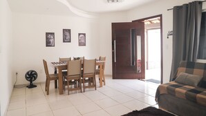 A living room with a dining area, a sofa, a fan, and a door leading to an outdoor area. - Casa de Praia Pet Friendly com Churrasqueira e Ar (Rio das Ostras)