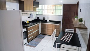A compact kitchen with wooden cabinets, a black countertop, and a small dining area with a striped placemat. - Casa de Praia Pet Friendly com Churrasqueira e Ar (Rio das Ostras)