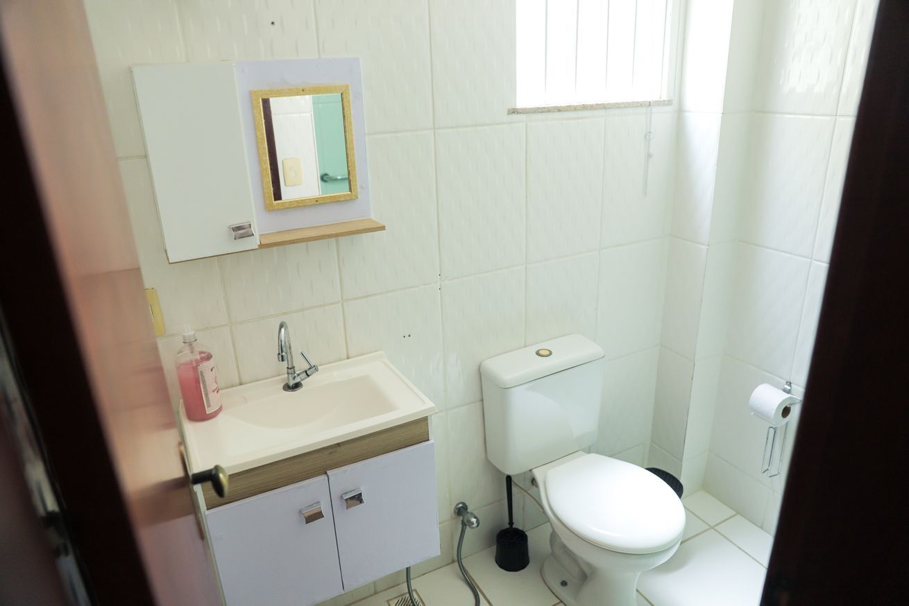 A small bathroom with a white sink, a mirror, a toilet, and a window.